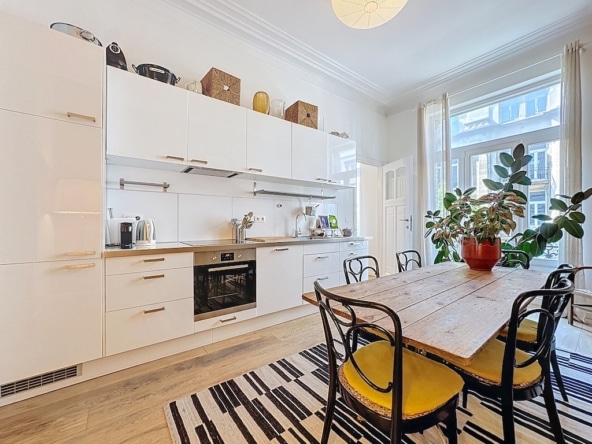Cuisine moderne lumineuse avec mobilier blanc, table en bois et touches de couleur chaleureuses.