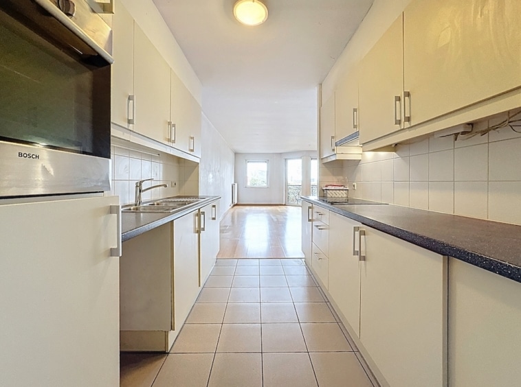 Cuisine moderne lumineuse avec meubles blancs, plan sombre et grandes fenêtres laissant entrer la lumière