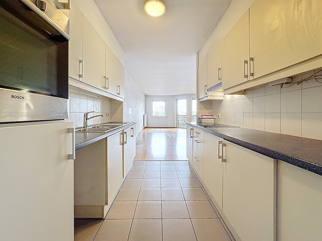 Cuisine moderne lumineuse avec meubles blancs, plan sombre et grandes fenêtres laissant entrer la lumière