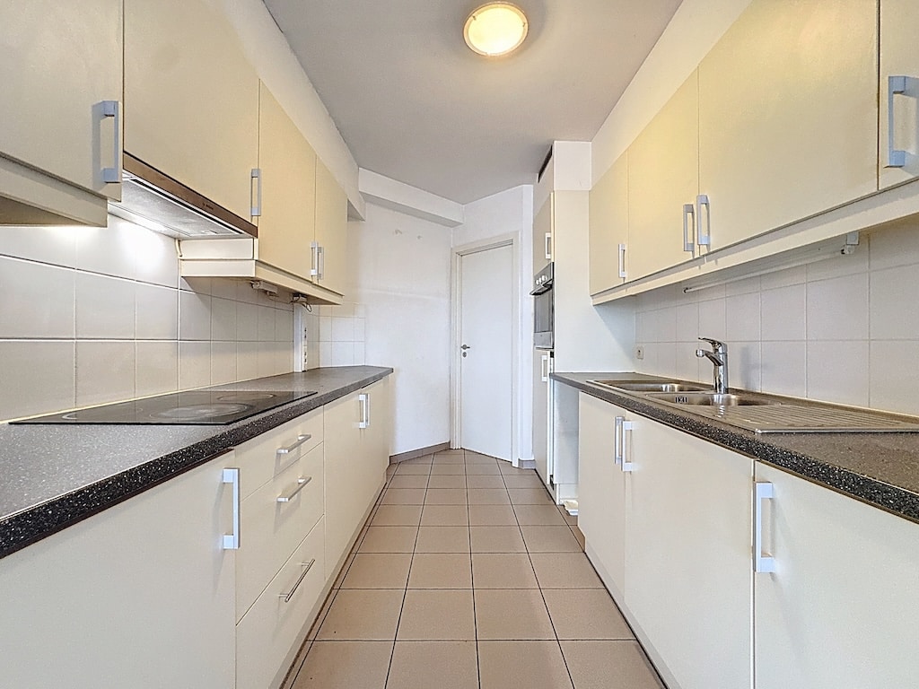 Cuisine moderne minimaliste avec armoires beige, plan de travail en granit foncé et carrelage blanc.