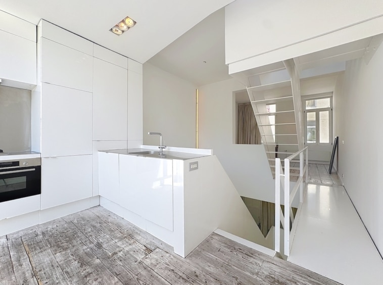 Cuisine moderne minimaliste lumineuse avec îlot, sols en bois clair et grande fenêtre naturelle.