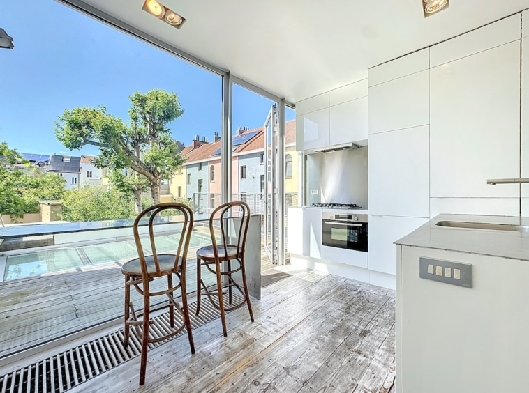Cuisine moderne lumineuse avec large fenêtre, mobilier épuré en bois, ambiance chaleureuse et ouverte.