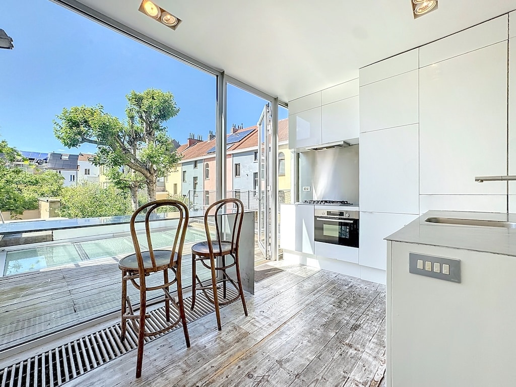 Cuisine moderne lumineuse avec large fenêtre, mobilier épuré en bois, ambiance chaleureuse et ouverte.