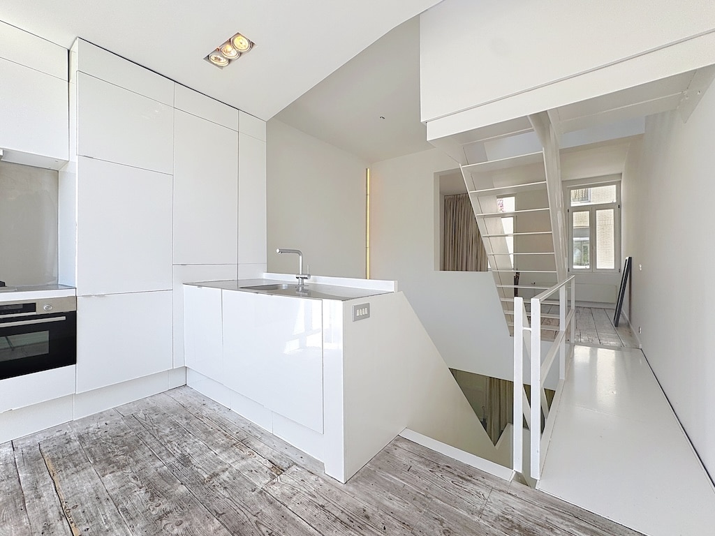 Cuisine moderne minimaliste lumineuse avec îlot, sols en bois clair et grande fenêtre naturelle.