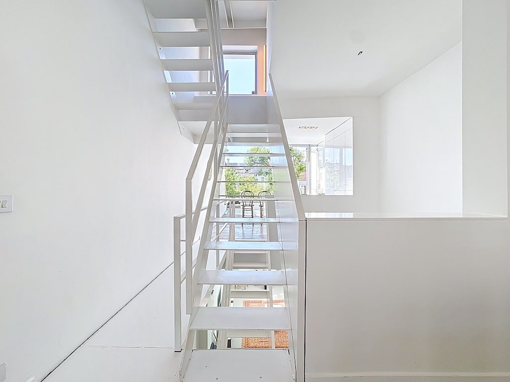 Escalier flottant blanc dans un intérieur minimaliste lumineux et moderne avec grandes fenêtres.