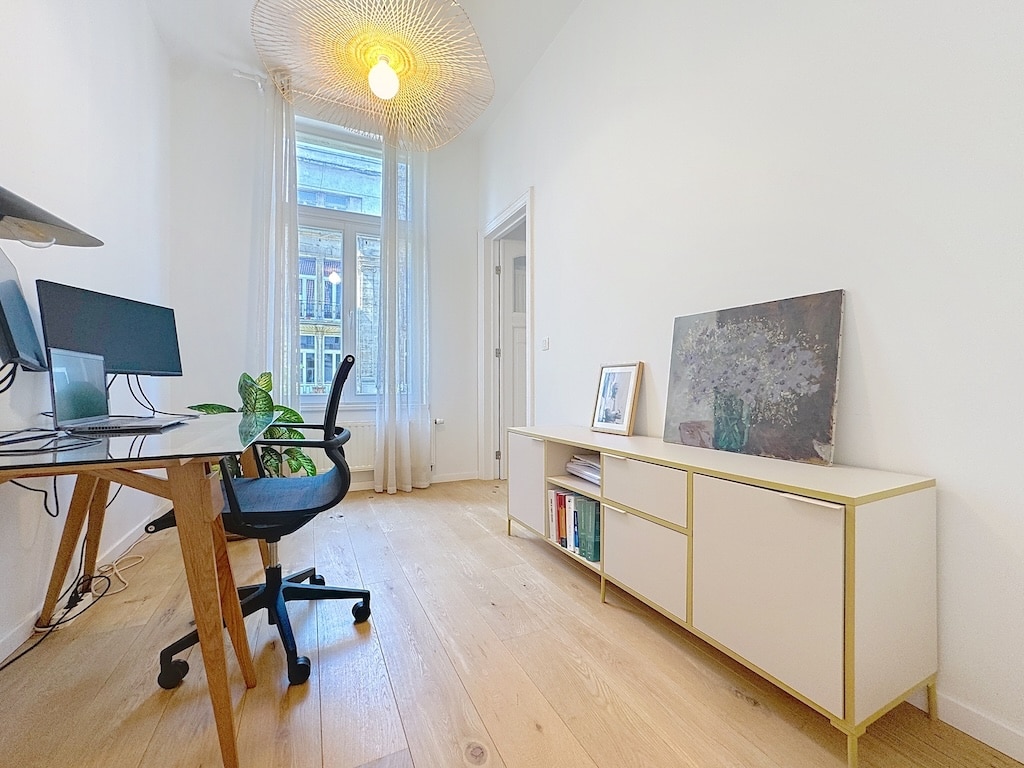Espace de travail moderne, lumineux, minimaliste avec bureau, écrans, plante, meuble doré et luminaire artistique.