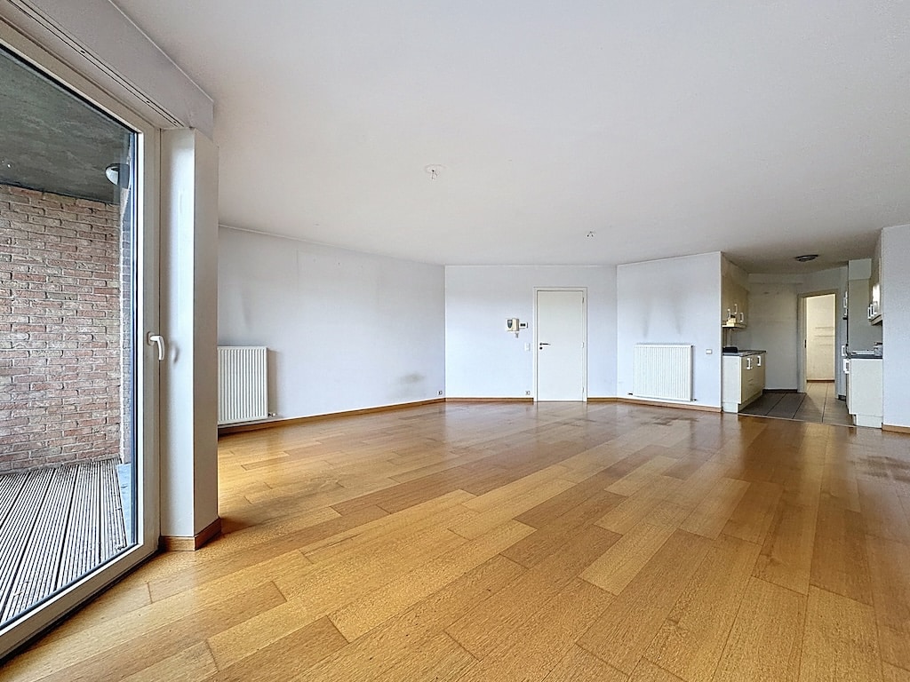 Salon moderne lumineux avec cuisine ouverte, sol en bois, grandes portes vitrées, vue agréable.