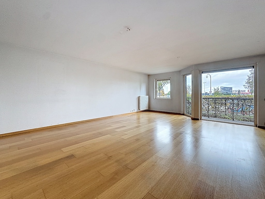 Espace lumineux avec balcon, sol en bois clair, murs blancs, idéal pour vivre ou travailler.