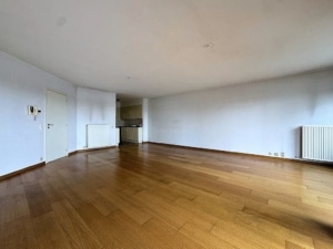 Espace lumineux minimaliste avec sol en bois clair, grande fenêtre et kitchenette fonctionnelle.