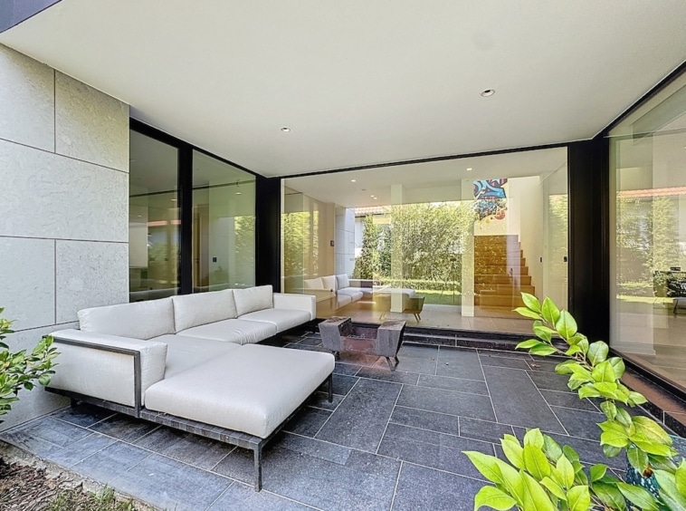 Espace extérieur moderne avec canapé, baie vitrée lumineuse et jardin verdoyant pour un style élégant