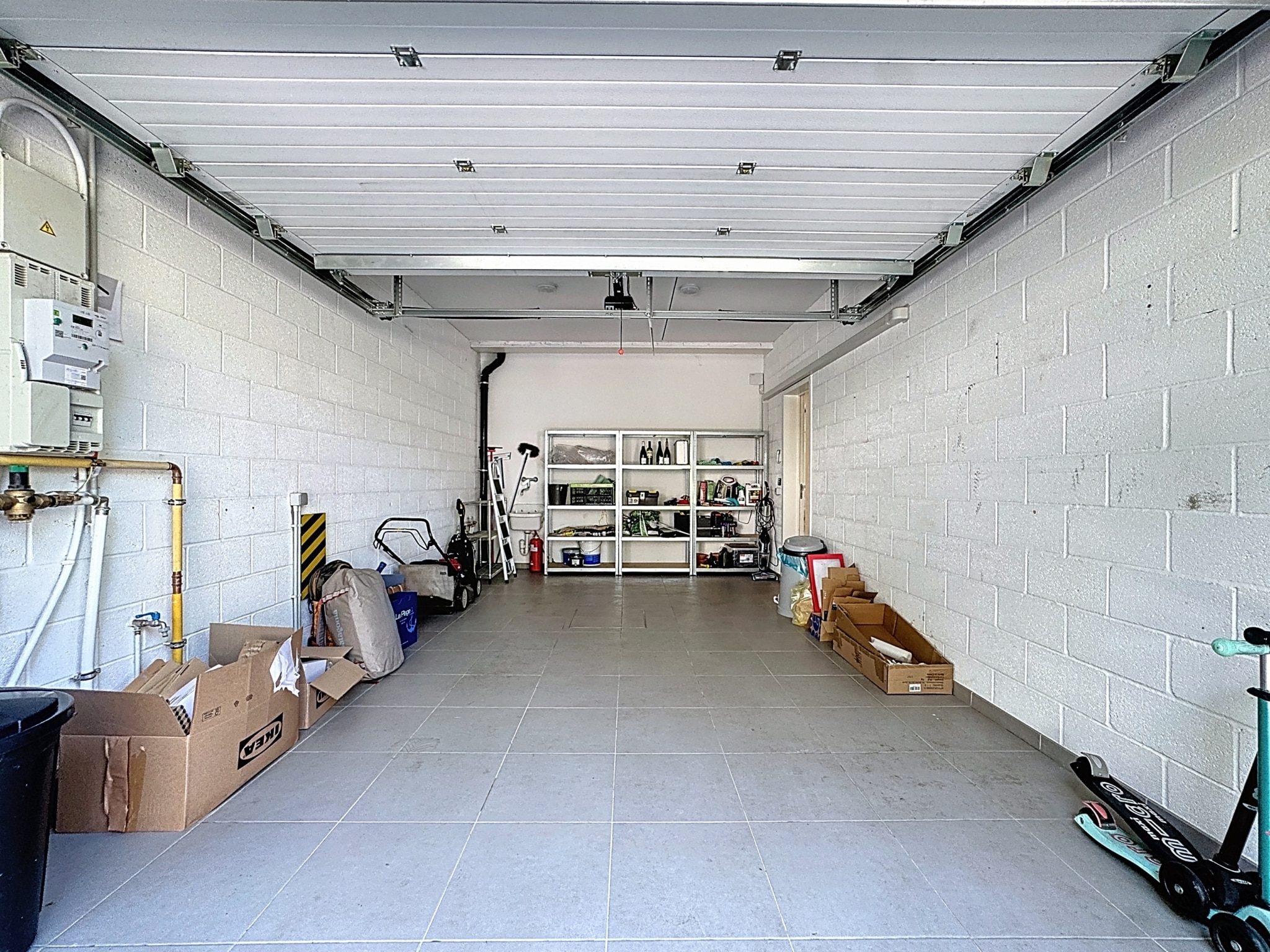 Garage lumineux, organisé avec étagères, cartons, scooter vert et espace de bricolage moderne.