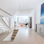 Intérieur moderne lumineux, escalier flottant blanc, œuvre d’art colorée, espace ouvert et design épuré.