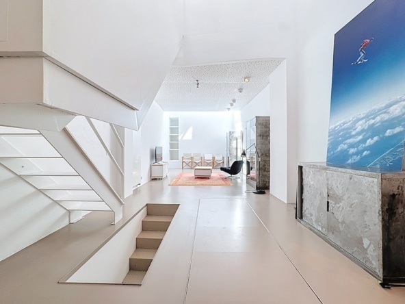 Intérieur moderne lumineux, escalier flottant blanc, œuvre d’art colorée, espace ouvert et design épuré.