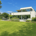 Maison moderne avec jardin, terrasse élégante, grandes fenêtres, ambiance contemporaine et paisible.