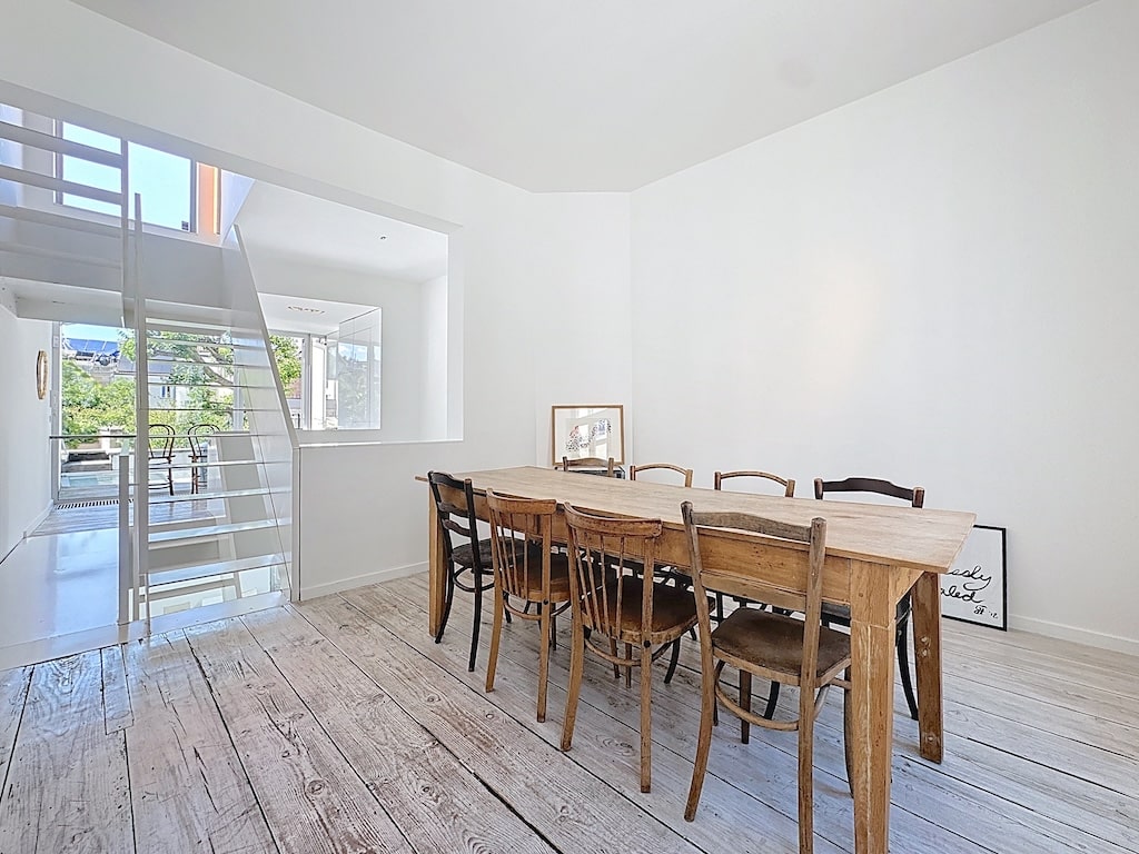 Salle à manger moderne avec table en bois, fenêtres panoramiques, escalier en verre et ambiance conviviale.