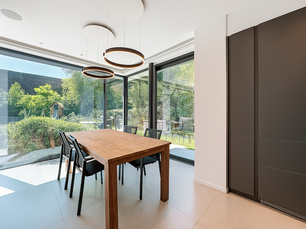 Salle à manger moderne avec grande baie vitrée, mobilier en bois et éclairage design.