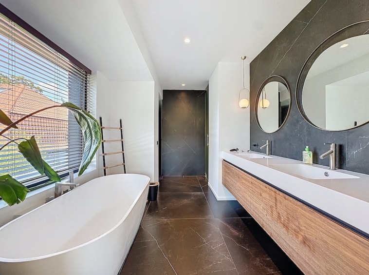 Salle de bain moderne avec baignoire blanche, miroirs ronds, touches naturelles et éclairage chaleureux.