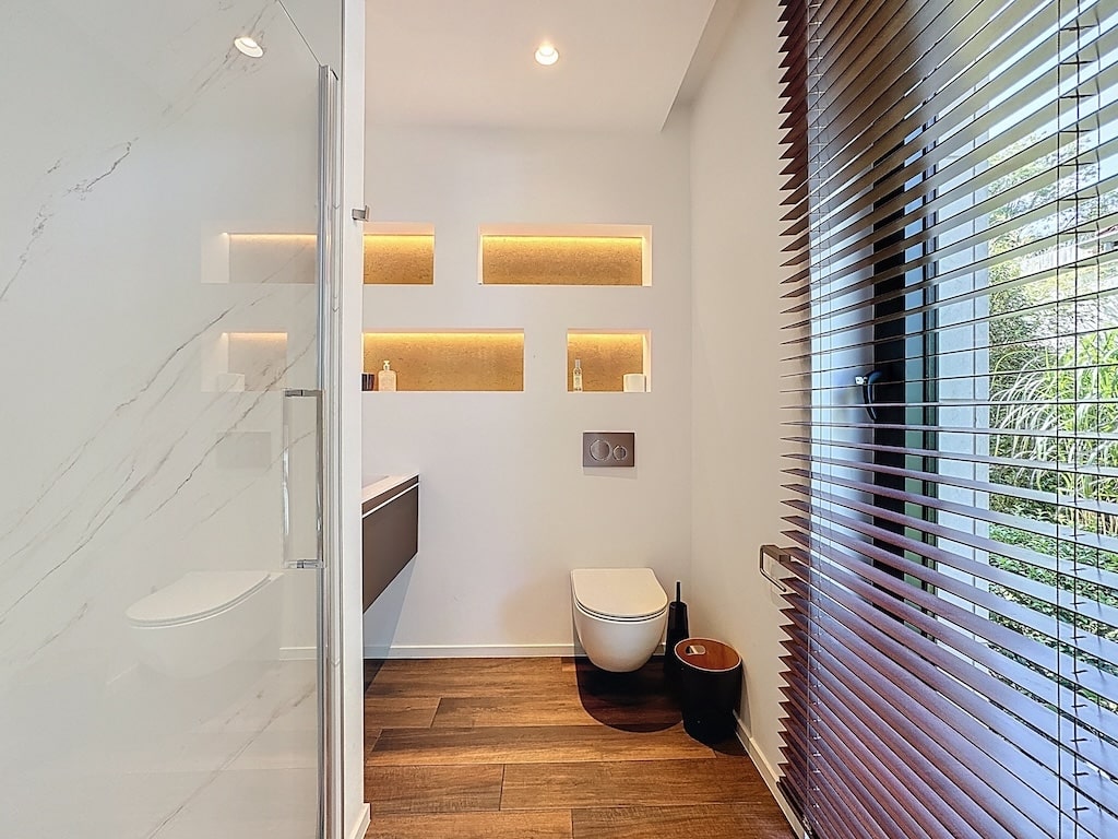 Salle de bain moderne avec douche en verre, rangements éclairés et ambiance élégante et lumineuse.