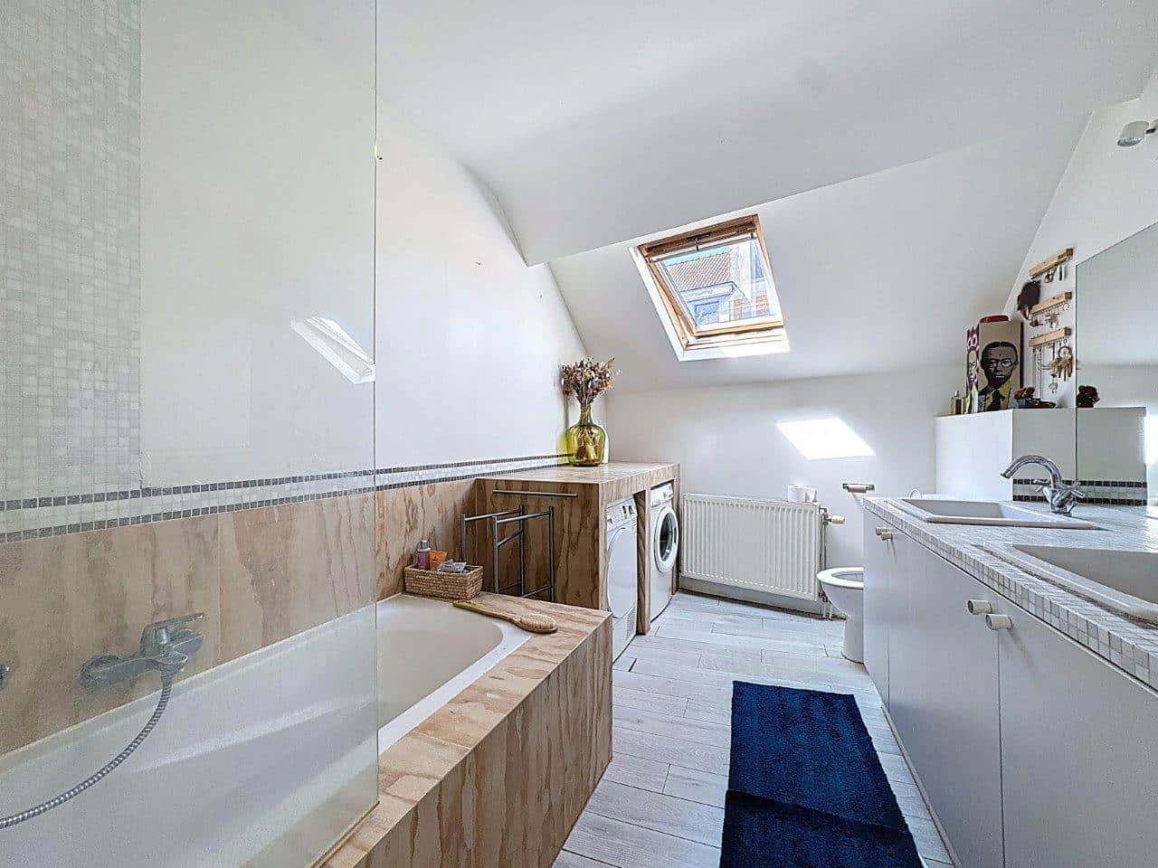 Salle de bain moderne en attique avec baignoire, douche en verre, lumière naturelle et design épuré.