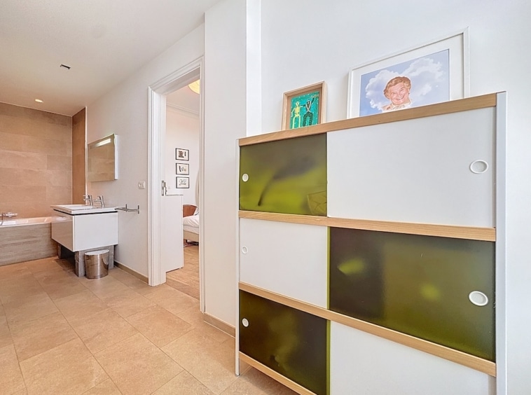 Salle de bain moderne lumineuse avec mobilier épuré, rangement coloré en verre, œuvres d’art encadrées.