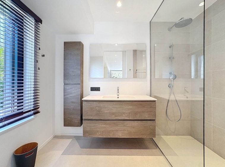 Salle de bain moderne lumineuse avec meuble en bois, douche en verre et design minimaliste.