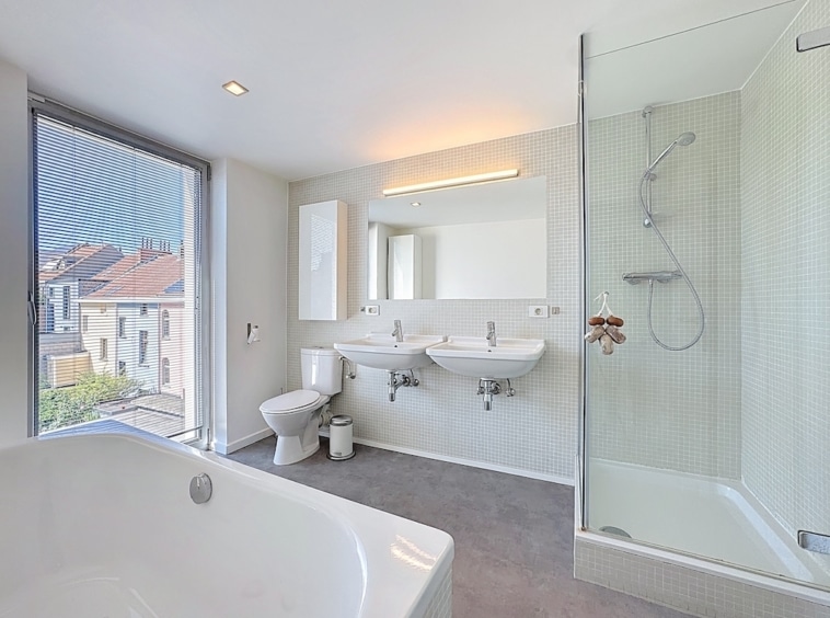 Salle de bain moderne avec douche en verre, baignoire spacieuse et double lavabo élégant.