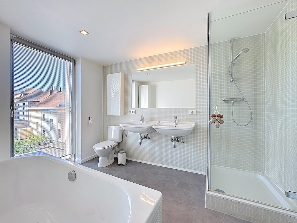 Salle de bain moderne avec douche en verre, baignoire spacieuse et double lavabo élégant.