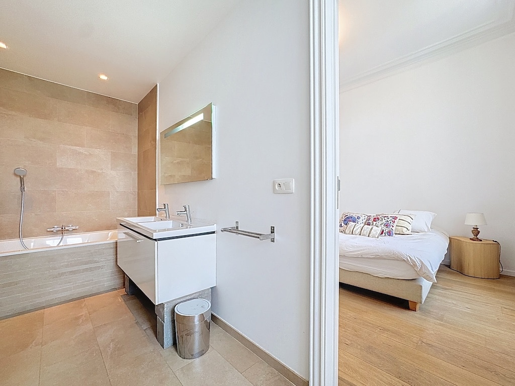 Salle de bain moderne lumineuse connectée à une chambre chaleureuse en bois naturel.