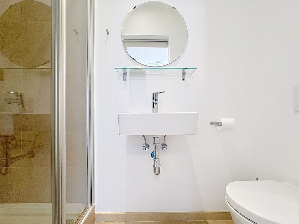 Salle de bain minimaliste moderne, blanche, lumineuse avec douche en verre et meubles épurés.