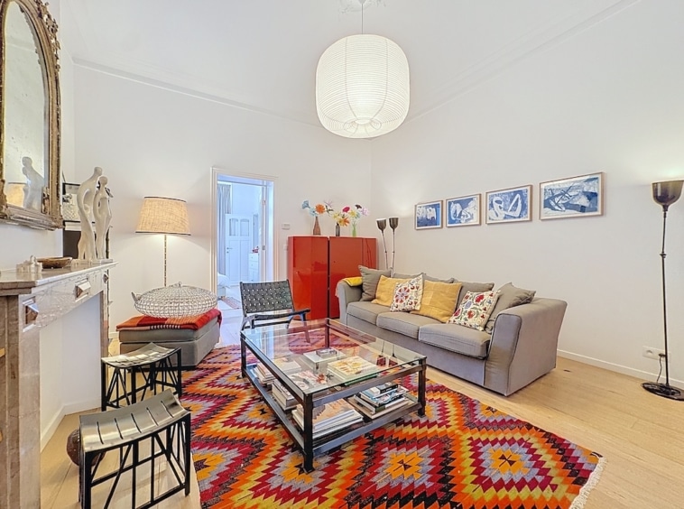 Salon moderne et cosy avec miroir orné, tapis géométrique et mobilier coloré.
