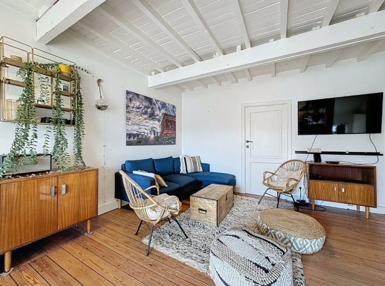 Salon moderne avec canapé bleu, fauteuils en rotin, plantes vertes, décoration élégante.