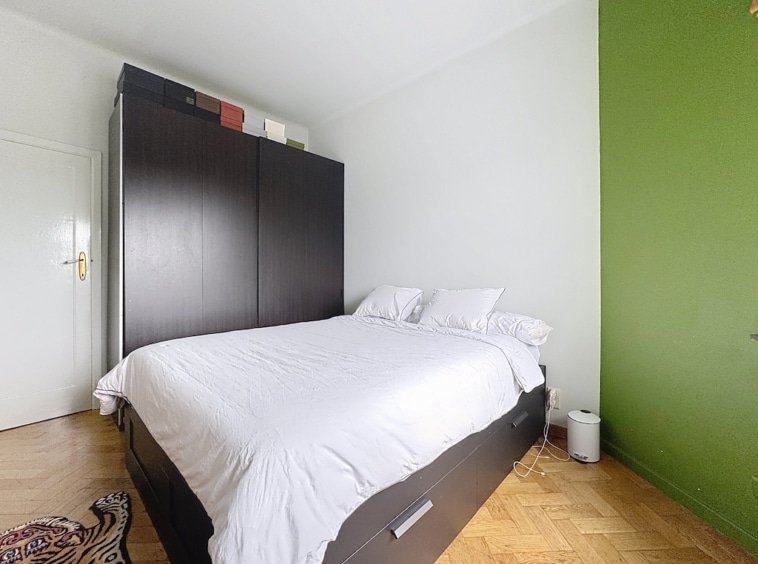 Chambre moderne avec lit blanc, mur vert vif, armoire noire et tapis rond à motifs.