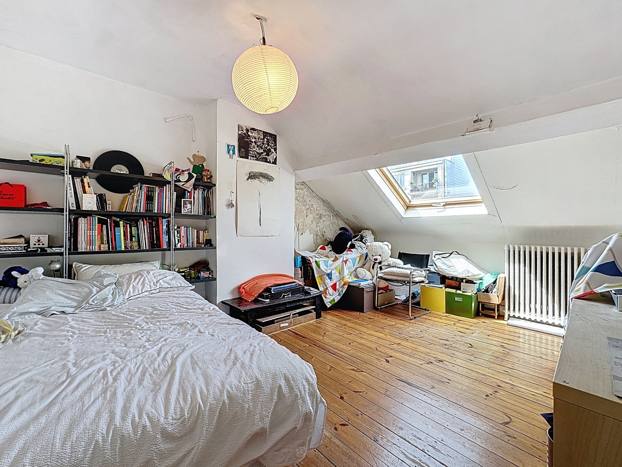 Espace attic lumineux, cosy et éclectique avec lit, bibliothèque, bureau et désordre charmant.