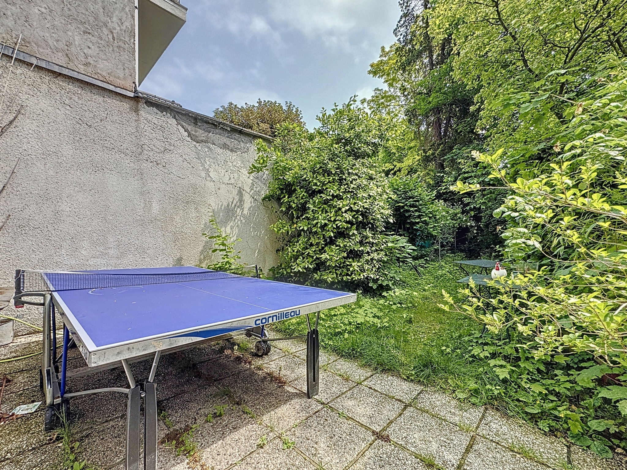 Coin privé avec table de ping-pong et jardin verdoyant, idéal pour détente et jeux en plein air.
