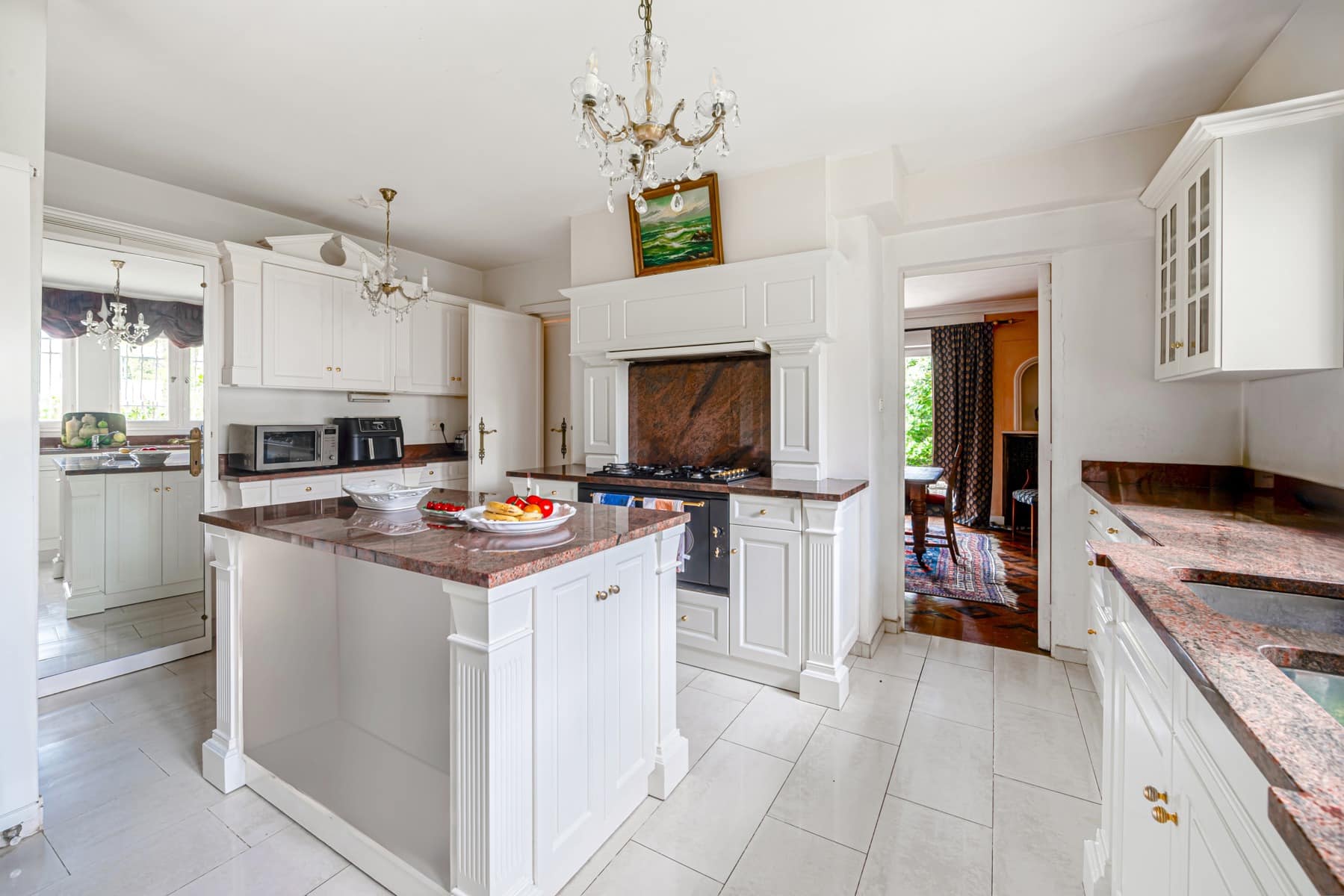 Cuisine lumineuse avec îlot central en granite, armoires blanches et éclairage naturel.
