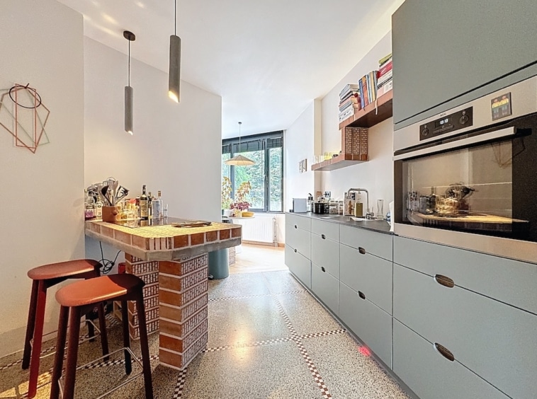 Cuisine moderne lumineuse avec îlot coloré, rangement élégant, et éclairage suspendu naturel.