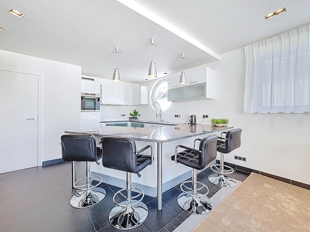 Cuisine moderne avec îlot noir, mobilier blanc épuré et tabourets en chrome élégants.