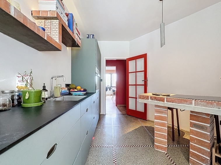 Cuisine moderne avec porte rouge, espace convivial, éléments en briques et design épuré.