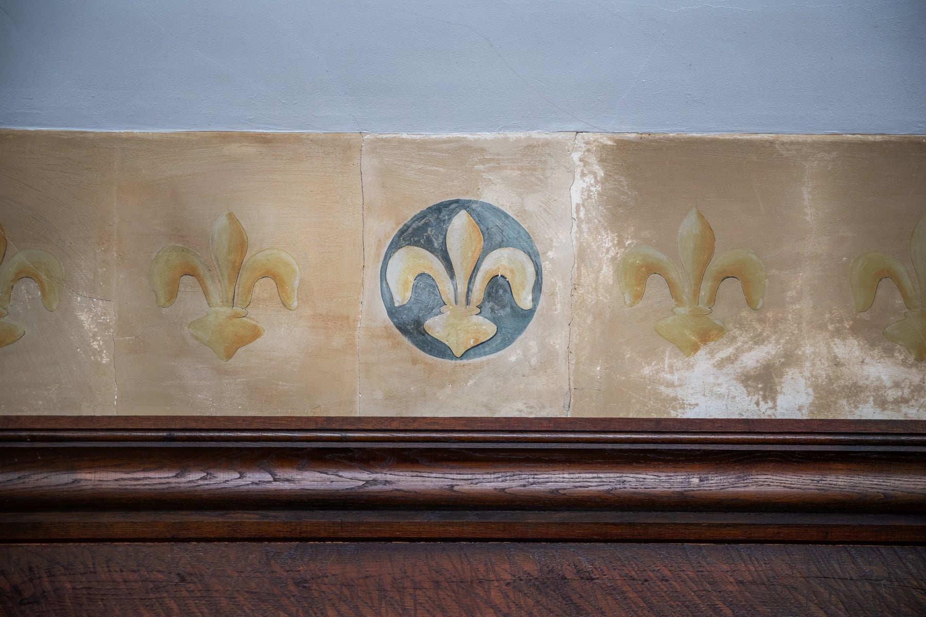 Décor mural élégant avec motifs de fleurs-de-lis dorées, cercle bleu et bande en bois sombre.