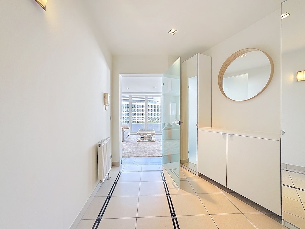 Entrée moderne et lumineuse avec miroir rond, mobilier épuré et portes en verre vers le séjour.