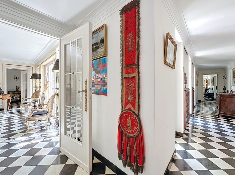 Hall élégant avec sol damier noir et blanc, murs blancs, œuvres colorées et coin salon accueillant.
