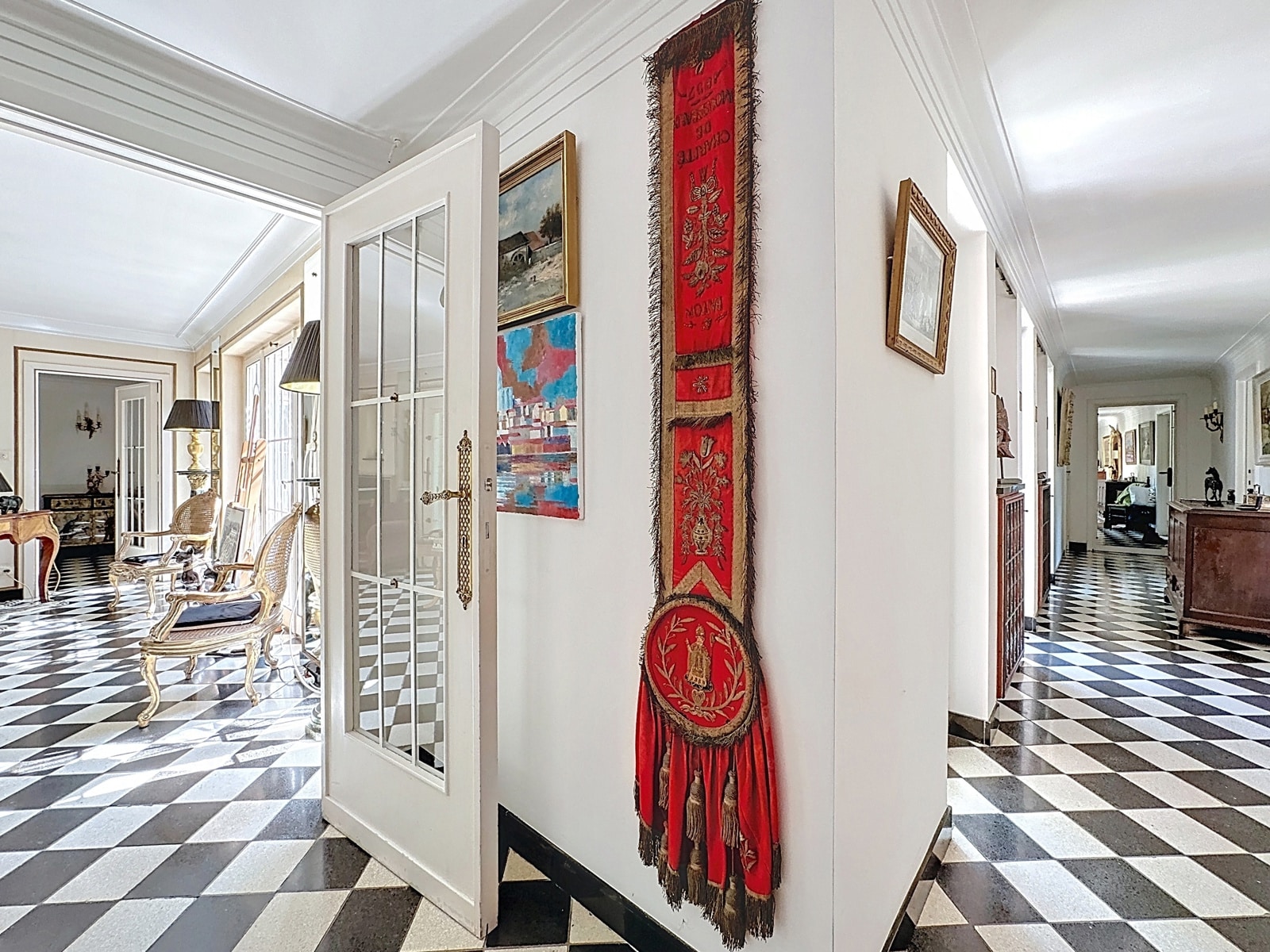 Hall élégant avec sol damier noir et blanc, murs blancs, œuvres colorées et coin salon accueillant.