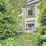 Jardin calme avec chemin bordé de verdure et fenêtre éclairée pour détente en plein air.