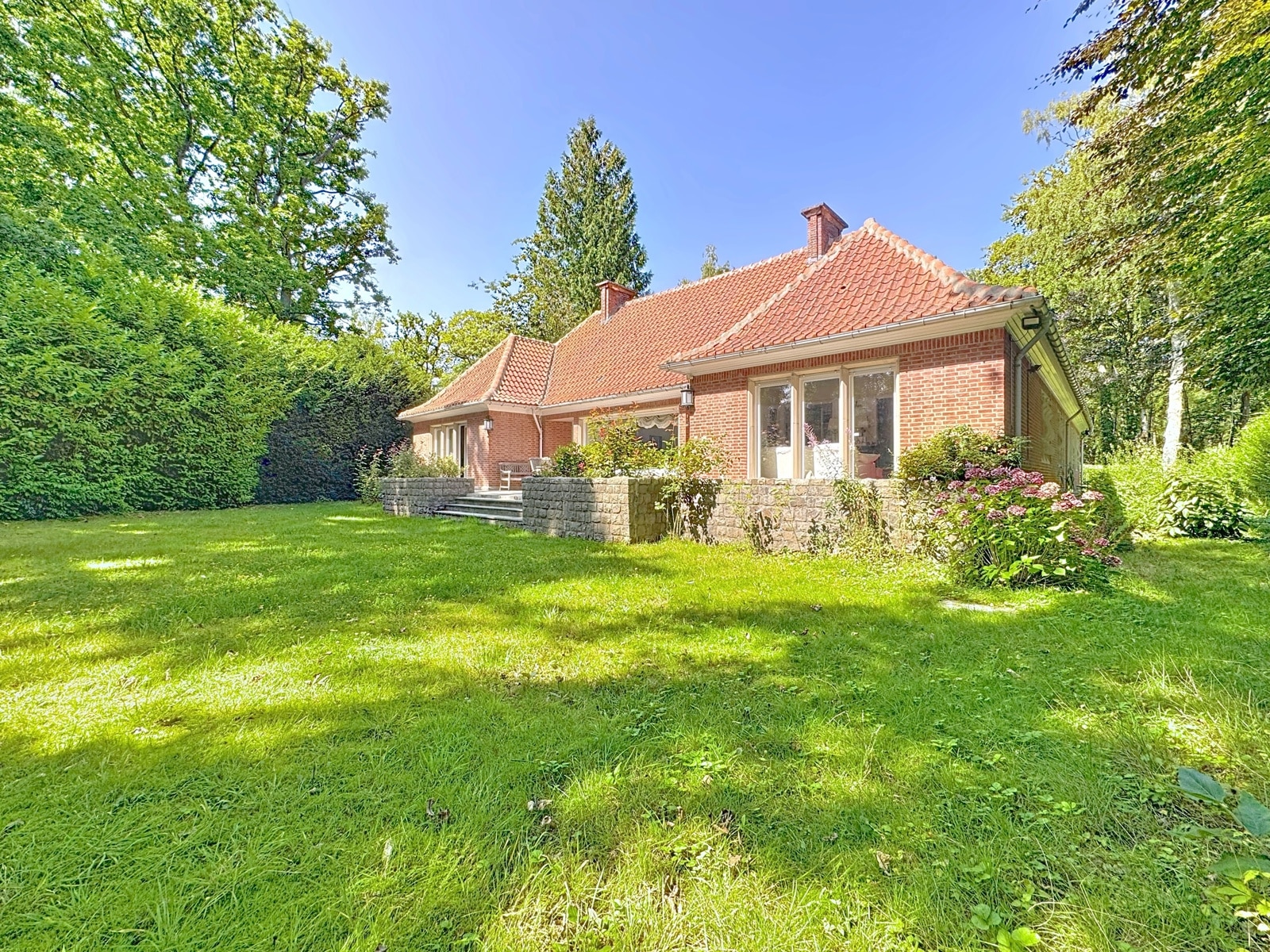 Maison de campagne chaleureuse avec jardin fleuri, arbre et soleil, ambiance paisible et accueillante.