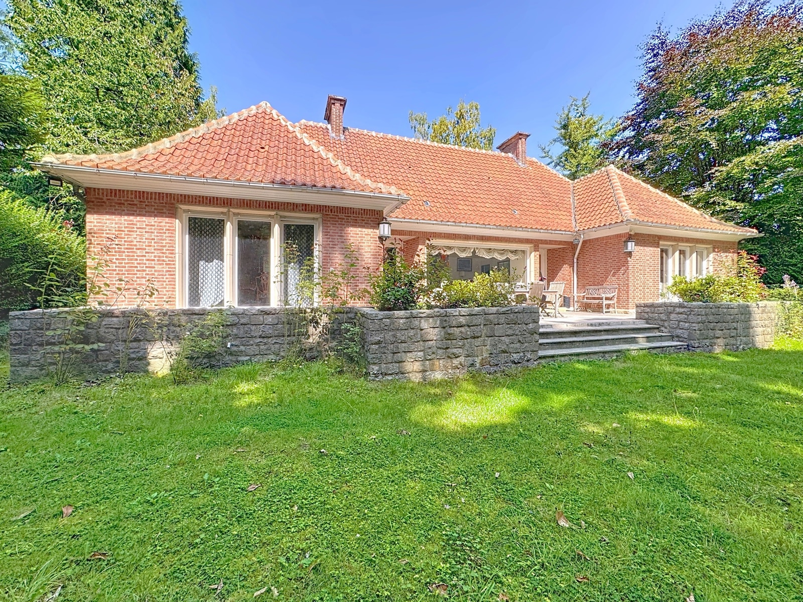 Maison rustique avec jardin verdoyant, fenêtres lumineuses, toiture en tuiles rouges et ambiance paisible.