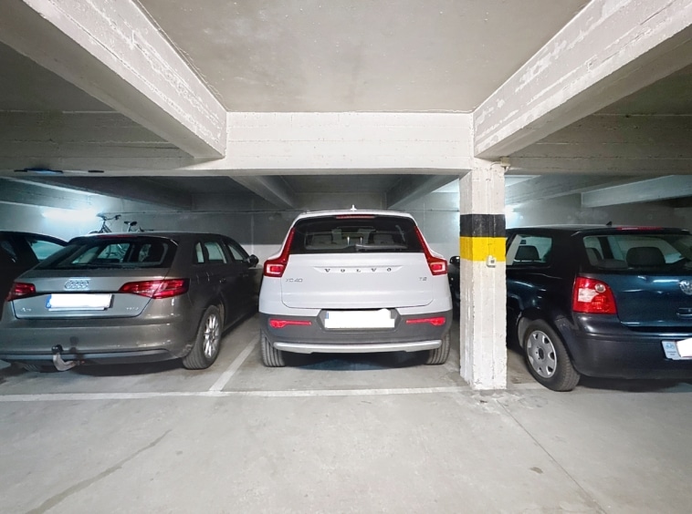 Parking souterrain avec SUV blanc, voitures gris et bleues, éclairage fluorescent et piliers en béton.