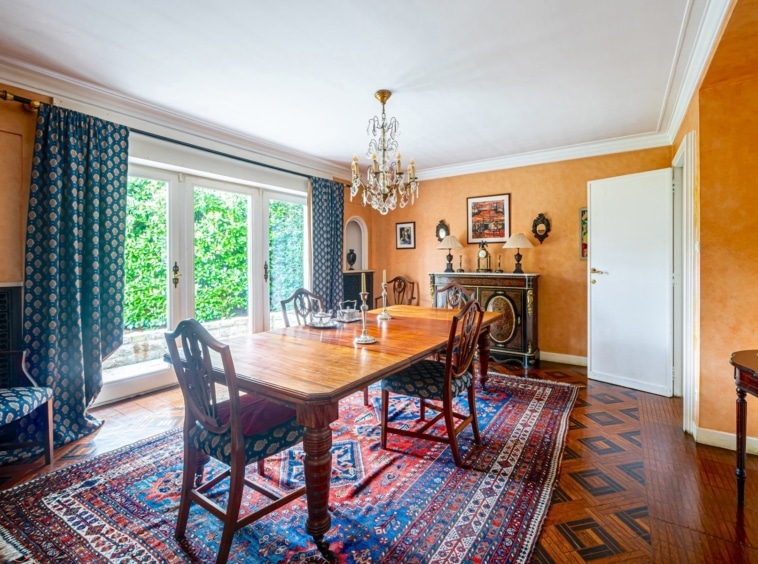 Salle à manger chaleureuse avec mobilier en bois, tapis persan, murs orange, luminaires et décor élégant.
