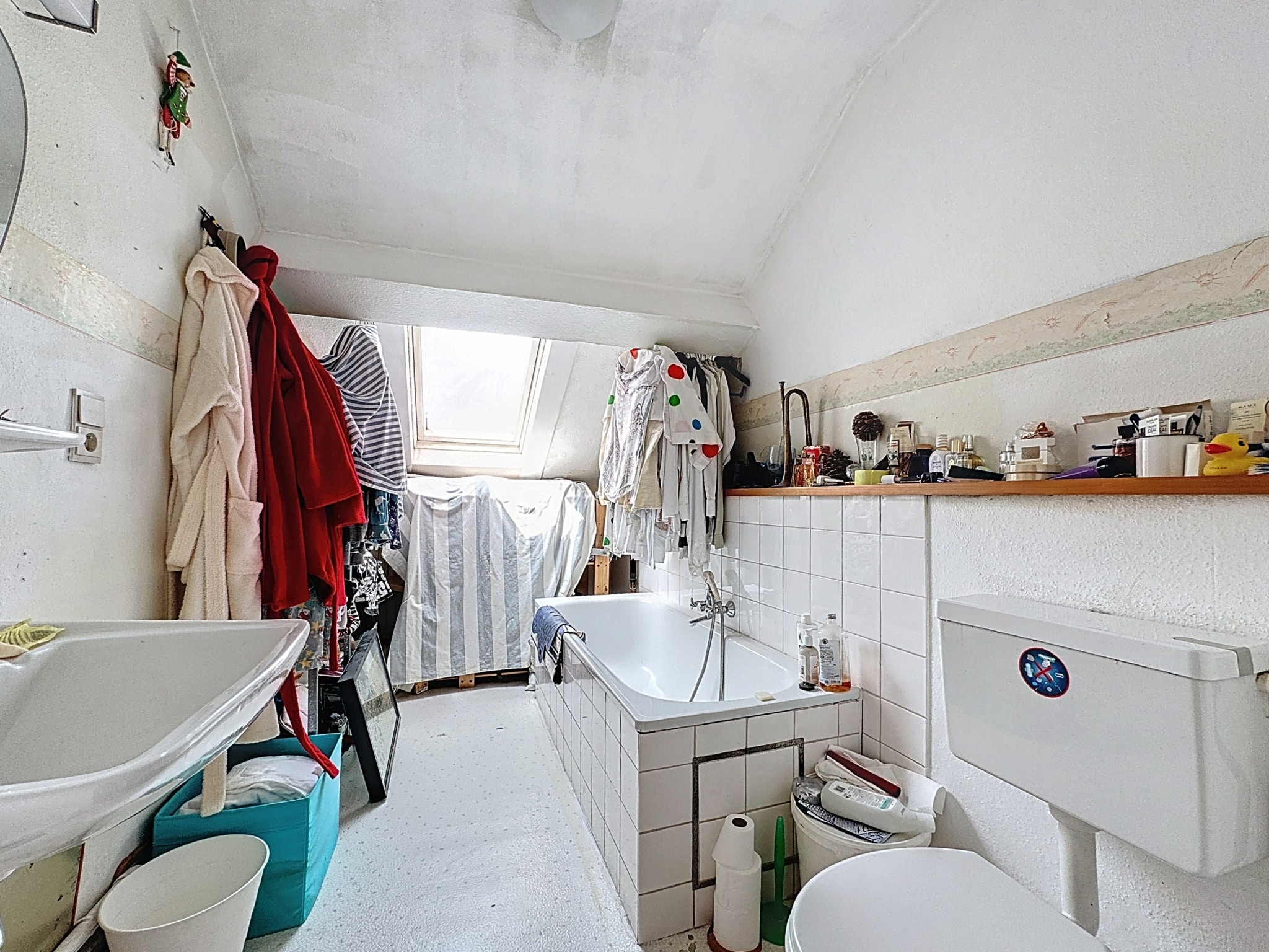 Salle de bain lumineuse, compacte, chaleureuse, avec baignoire, lavabo, toilettes et linge suspendu.