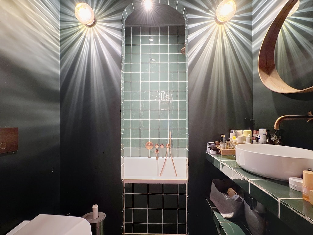 Salle de bain moderne avec baignoire blanche, murs verts profonds et éclairage chaleureux.