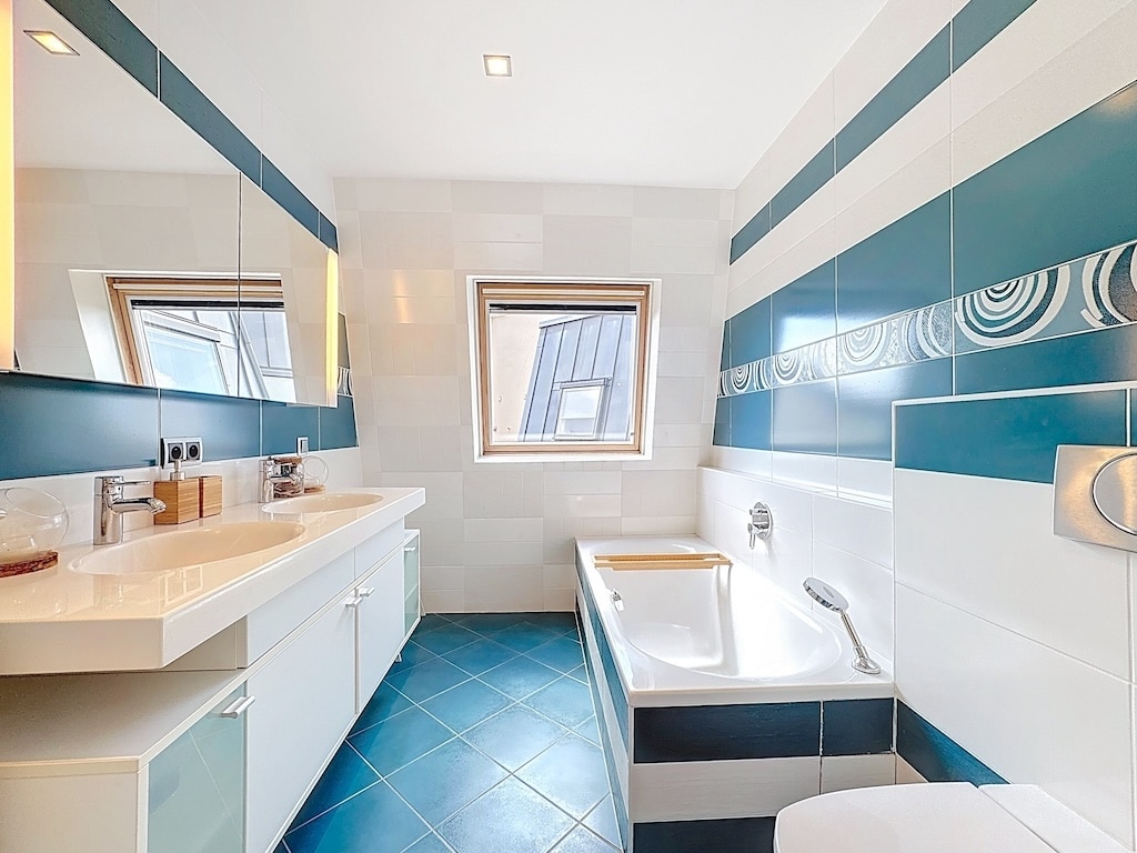 Salle de bain moderne avec murs teal, sol bleu foncé, baignoire minimaliste et éclairage naturel.